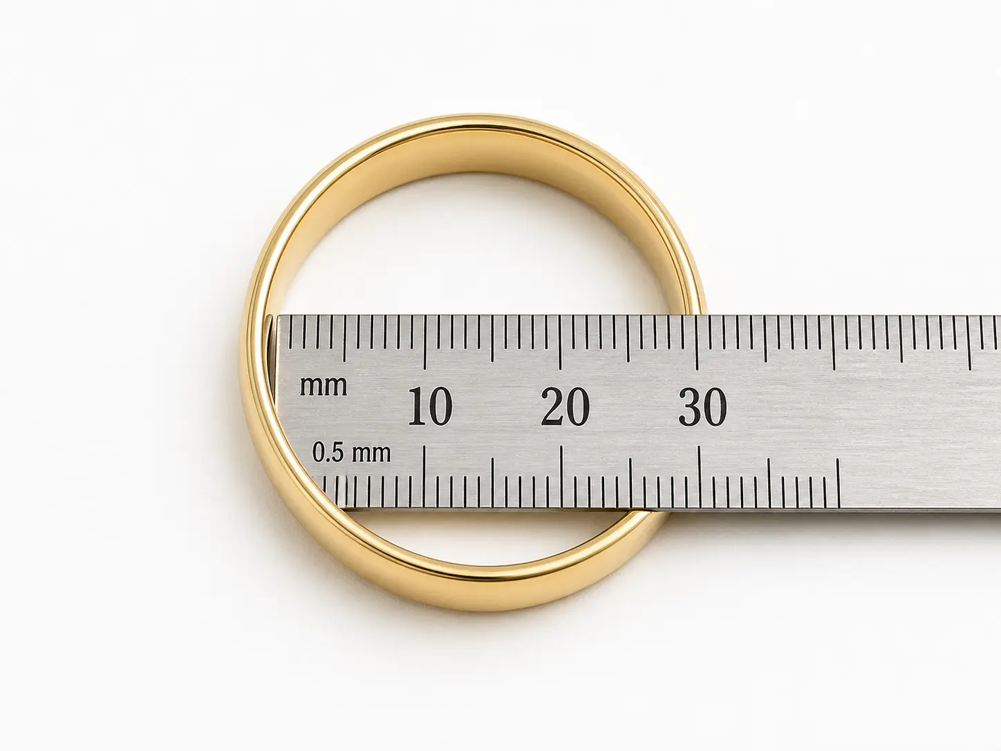 Plain gold ring lying flat on white surface with millimeter ruler positioned across internal diameter at widest point for ring size measurement