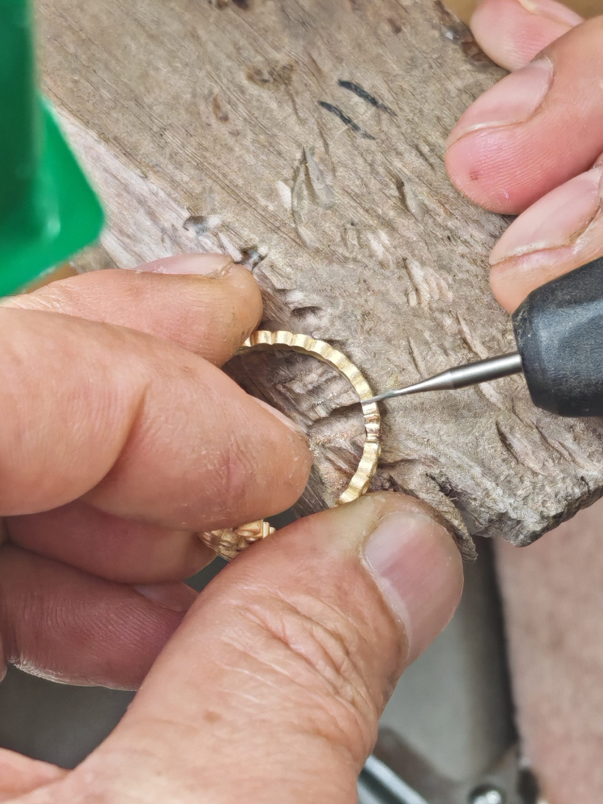 Jeweler hand cutting stone seats into a gold letter ring on a wooden bench pin