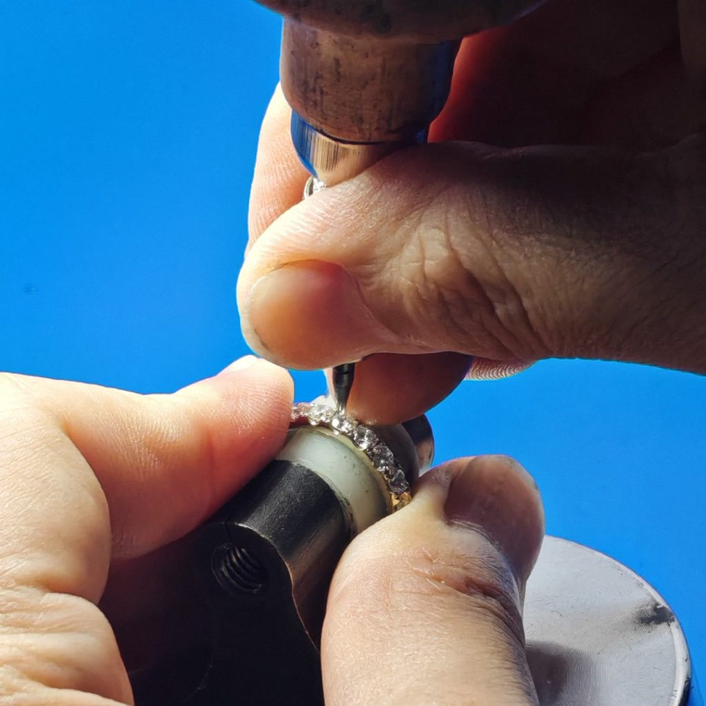 Setting a diamond into the 14K white gold half eternity band with a rotary graver at the bench