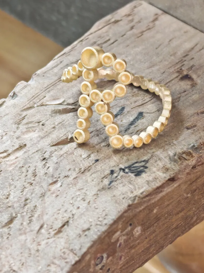 gold letter ring model resting on a wooden bench pin with the diamond seats cut and no stones set yet