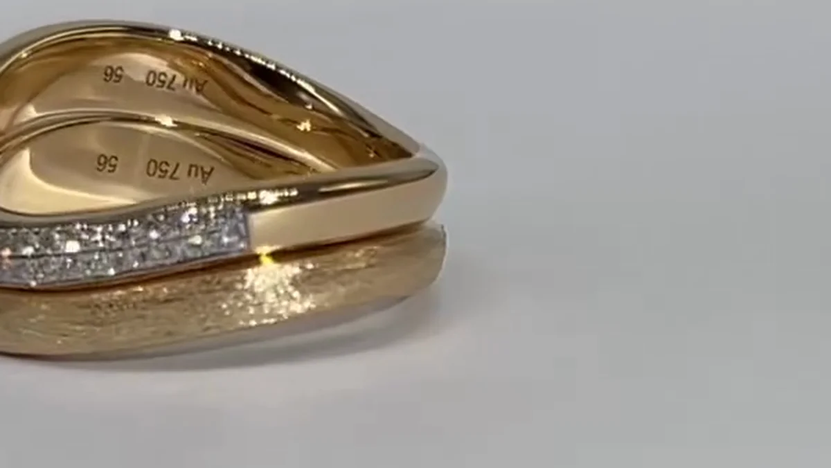 Inside of two 18K yellow gold wave bands stamped Au750 and size 56 on a polished surface, with the sandblasted outer face below