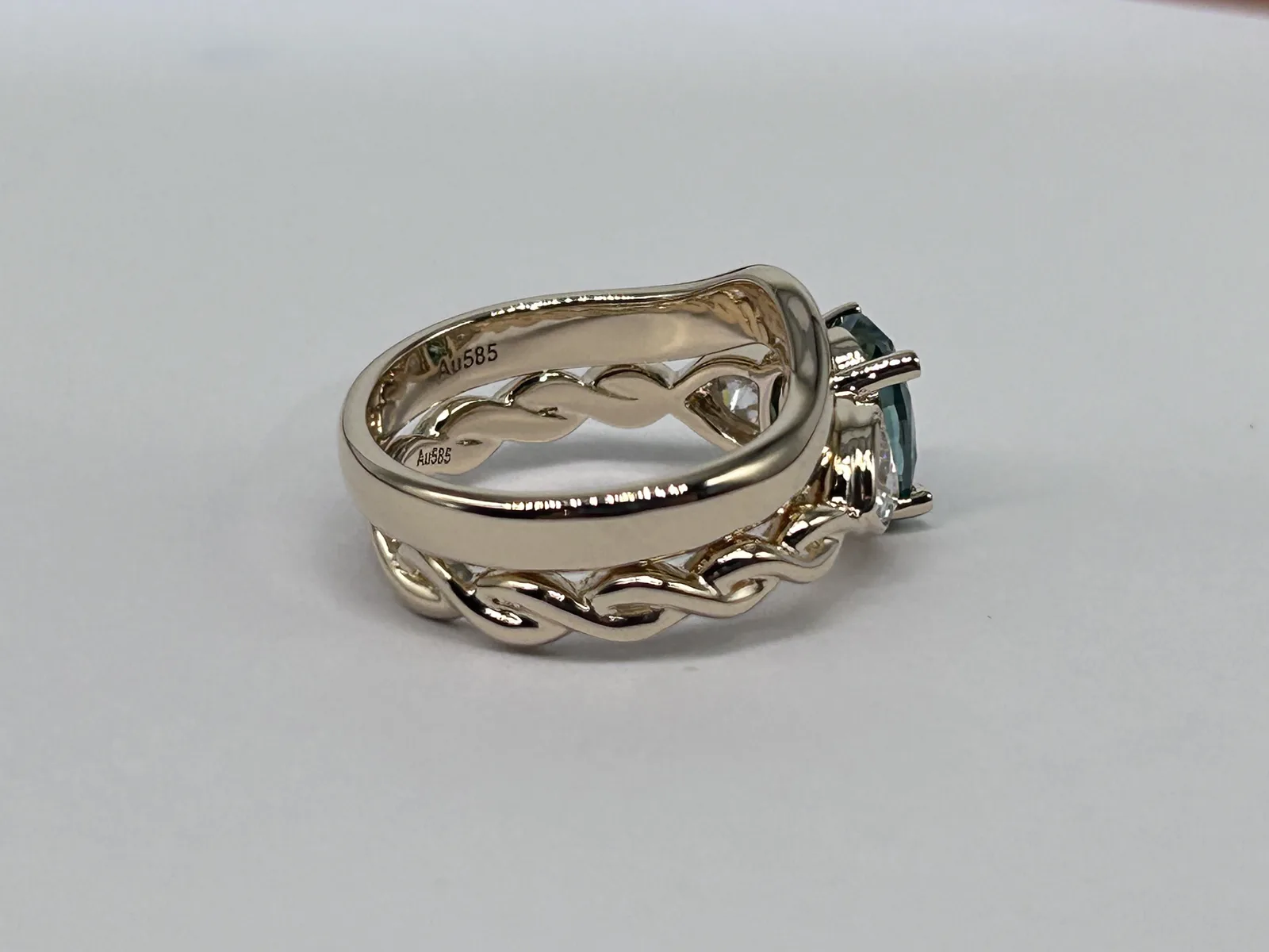 Side view of a polished 14K gold wedding band resting on the twisted shank of a three stone ring, both stamped Au585 inside