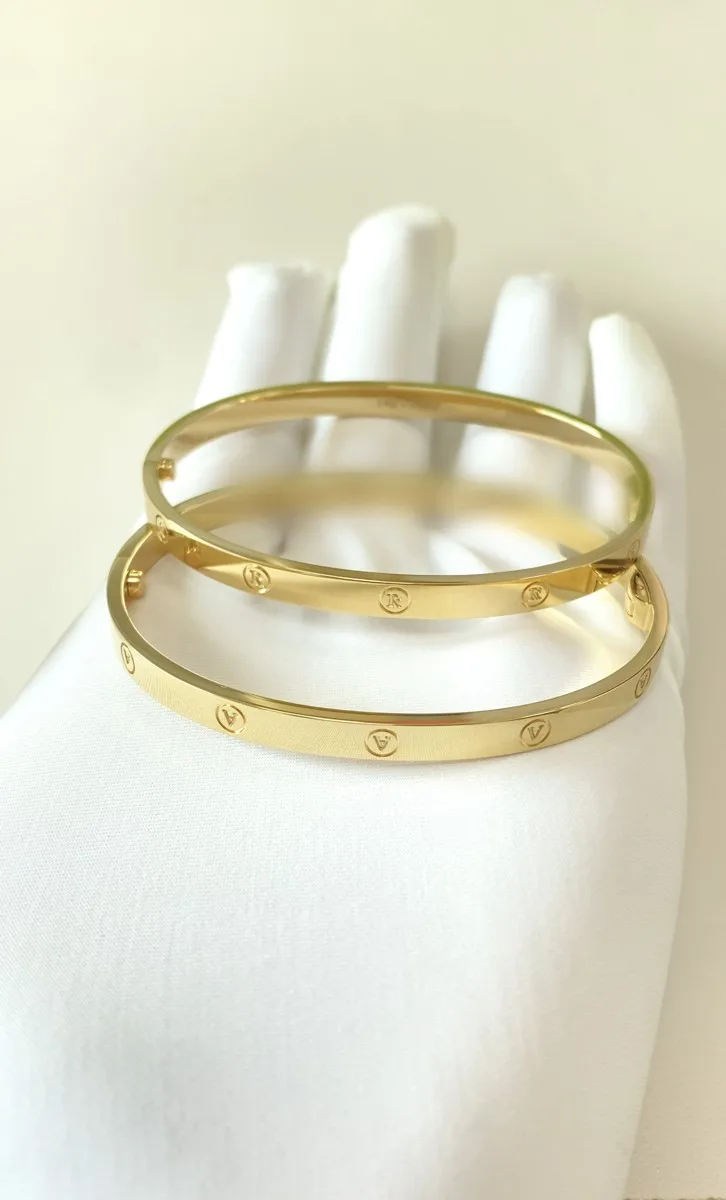 Finished pair of 14K yellow gold initial bangles, letters R and A, 2.2 mm thick, on a white glove
