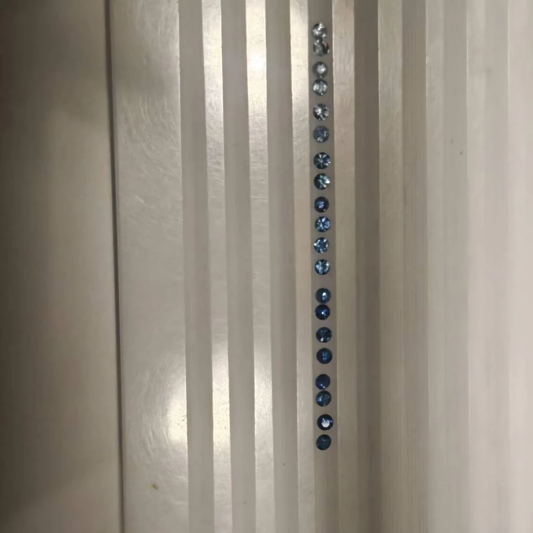 Round lab grown blue sapphires laid in a line in a grooved metal tray, pale stones at the top shading to deep blue at the bottom