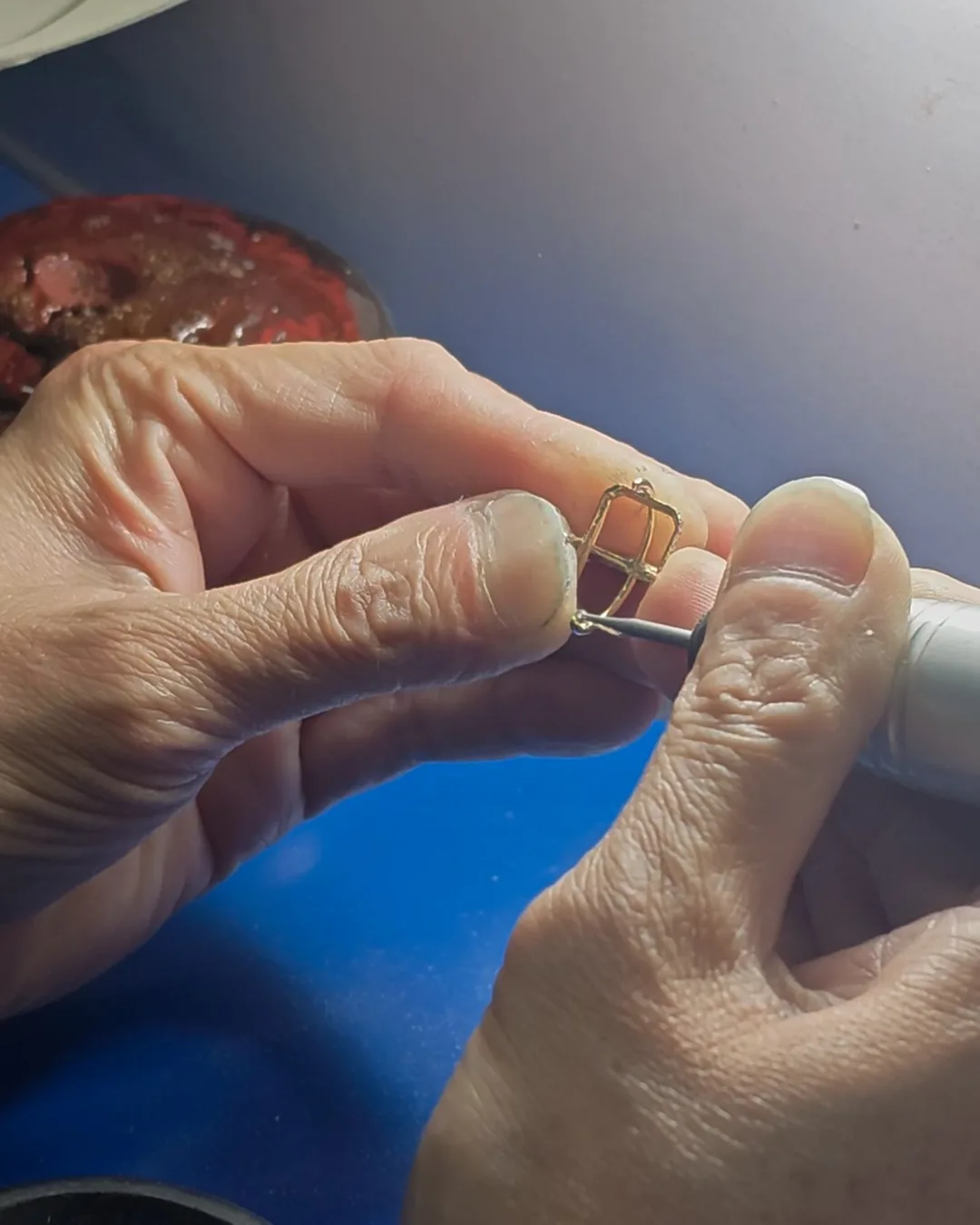 Empty prong frame for an emerald cut diamond being trimmed with a rotary tool at the bench before the stone is set