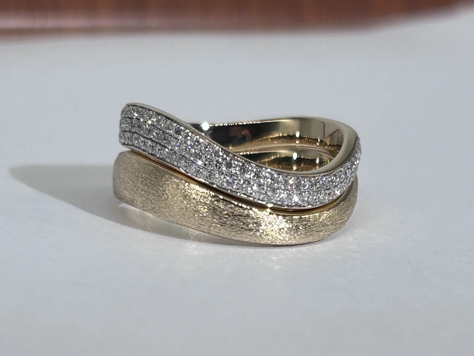 Two wave shaped 18K yellow gold bands stacked, a band with three rows of pavé diamonds above a sandblasted matte band