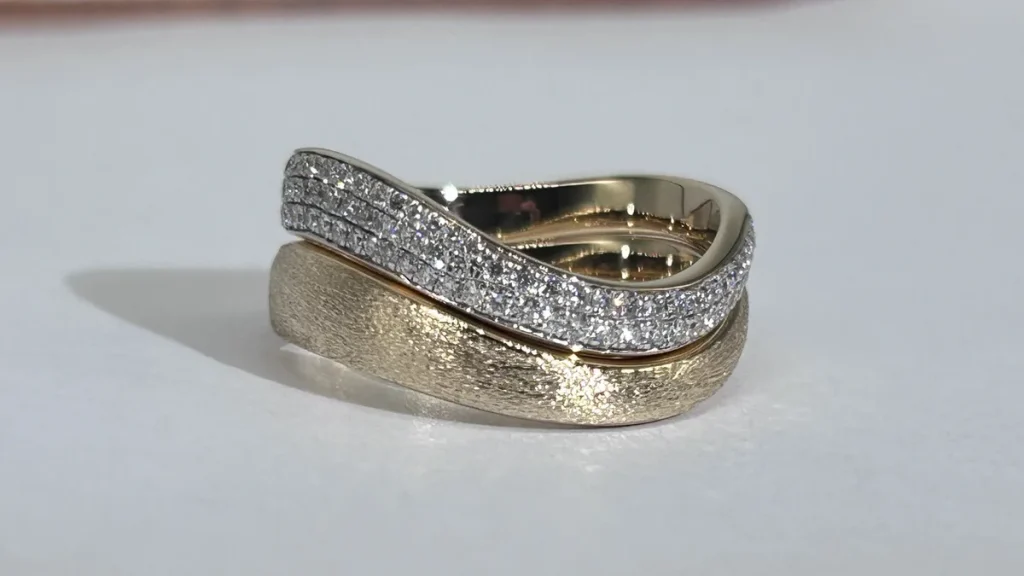 Sandblasted 18K yellow gold wave band stacked under a three row pavé diamond band on a white surface
