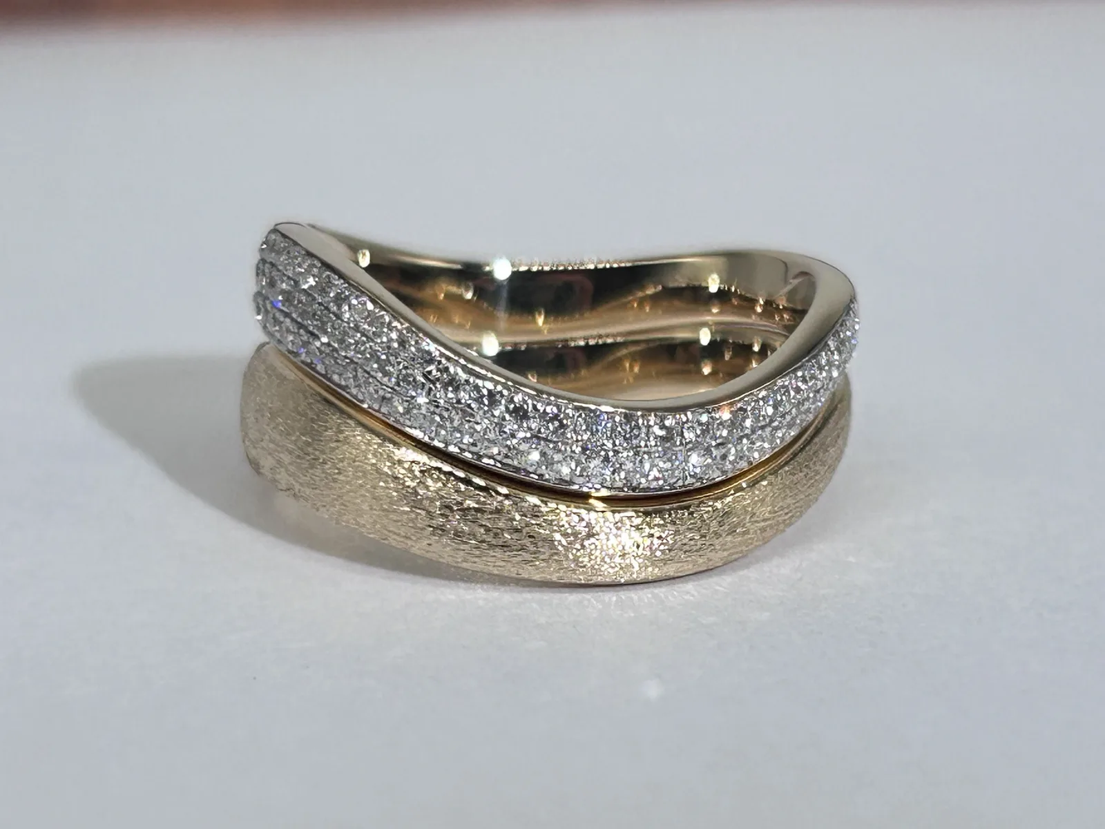 Side view of a sandblasted 18K yellow gold wave band under a pavé diamond band, showing the polished inside of the upper band