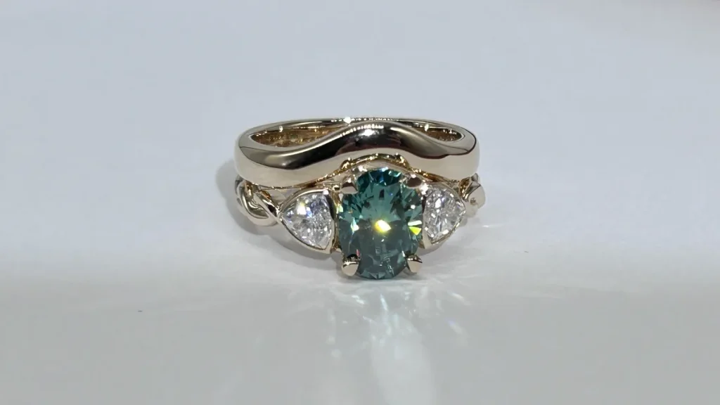 Curved 14K yellow gold wedding band fitted around a three stone engagement ring with a teal oval center and trillion side stones